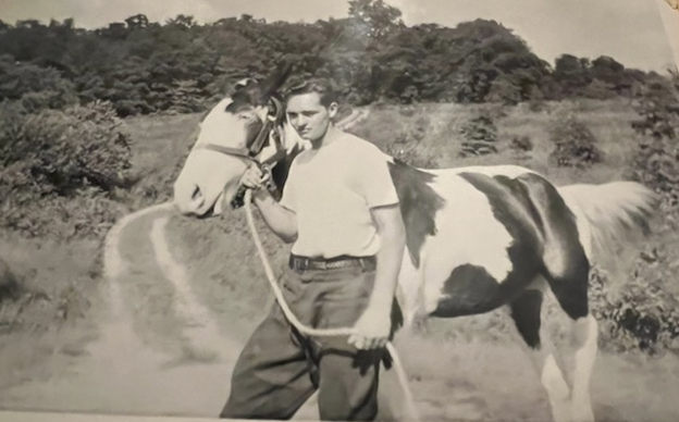 A young man is holding a horse in a field, capturing a moment of rural life and companionship.