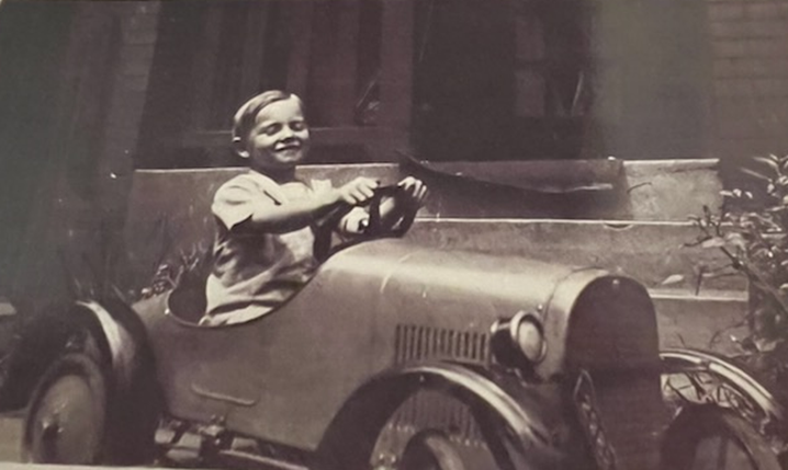 A cheerful boy drives a vintage toy car, smiling while enjoying a sunny afternoon.