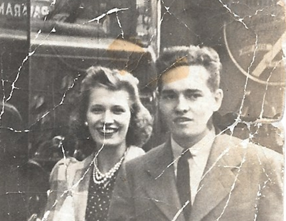 Two individuals dressed in classic clothing pose happily on a bustling city street.