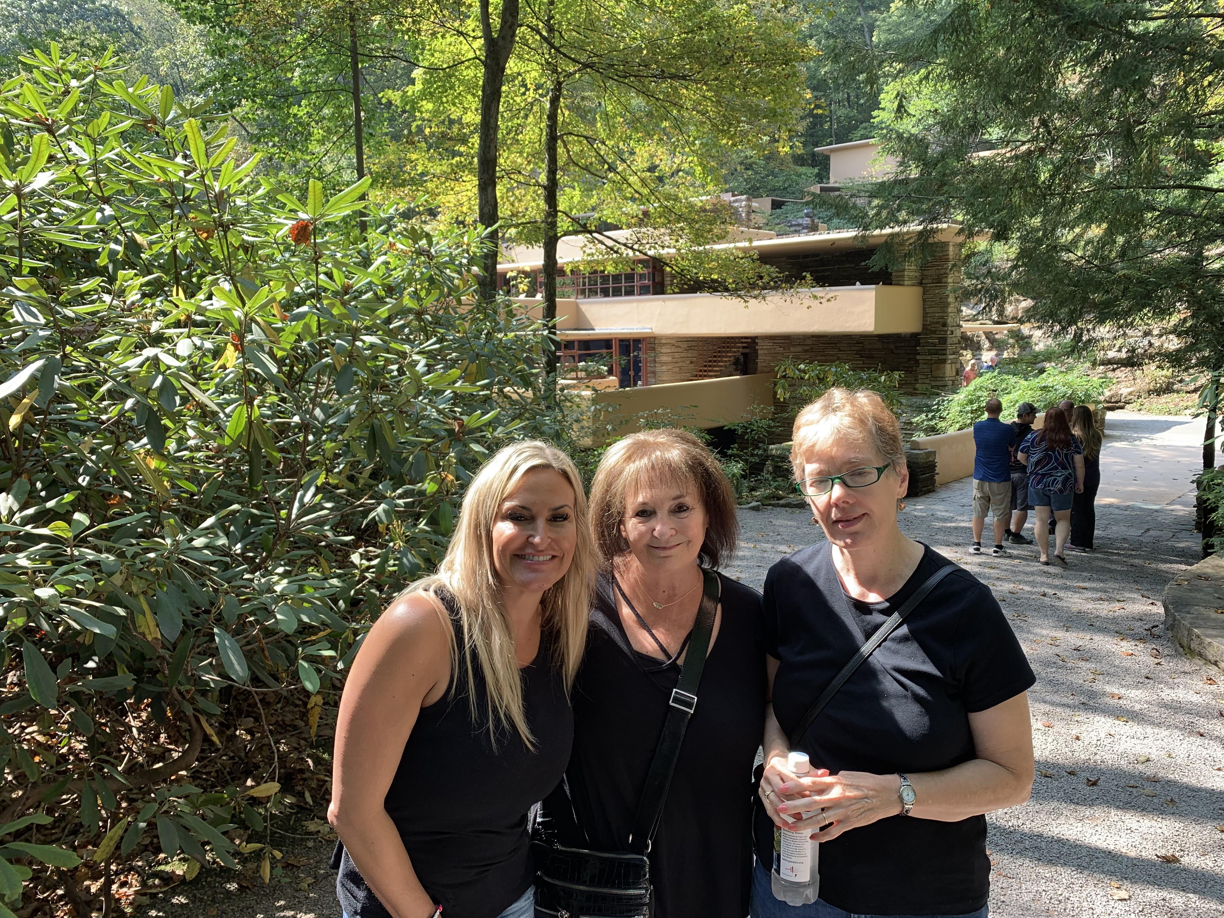 Three friends pose for a casual picture in a scenic outdoor setting surrounded by greenery.
