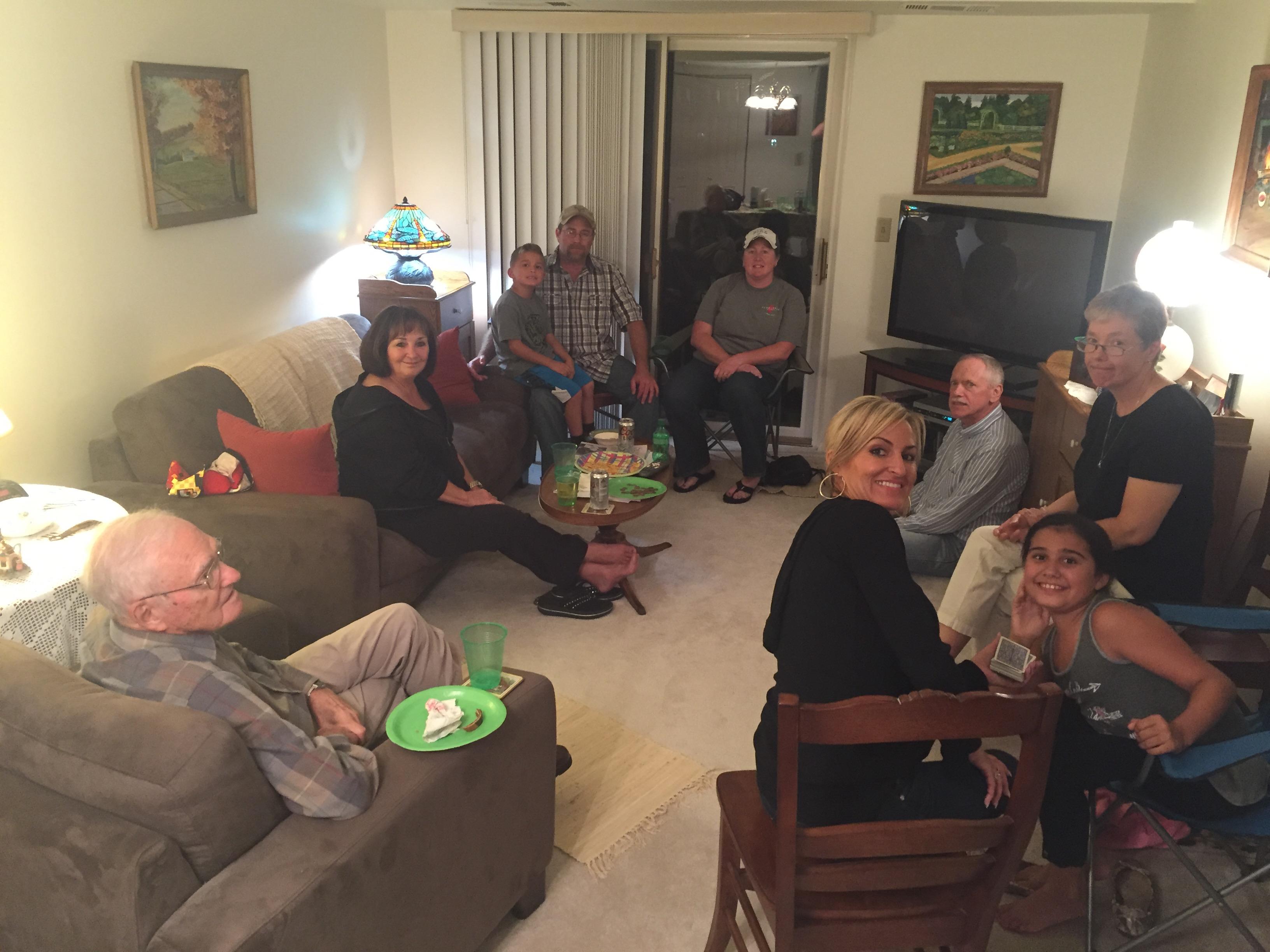 Group of friends laugh and share meals together in a warm living room during the evening.