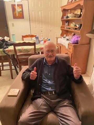 An elderly man expresses joy while seated in his chair, surrounded by home decor and furniture.