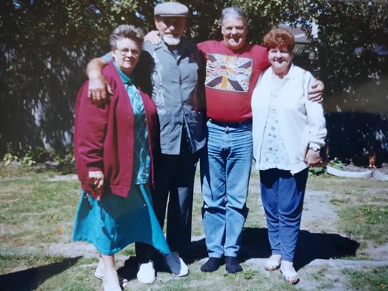 Four friends smile and pose together in a bright backyard during a joyful gathering.
