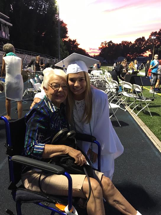 A woman in a graduation cap and gown hugging an elderly woman