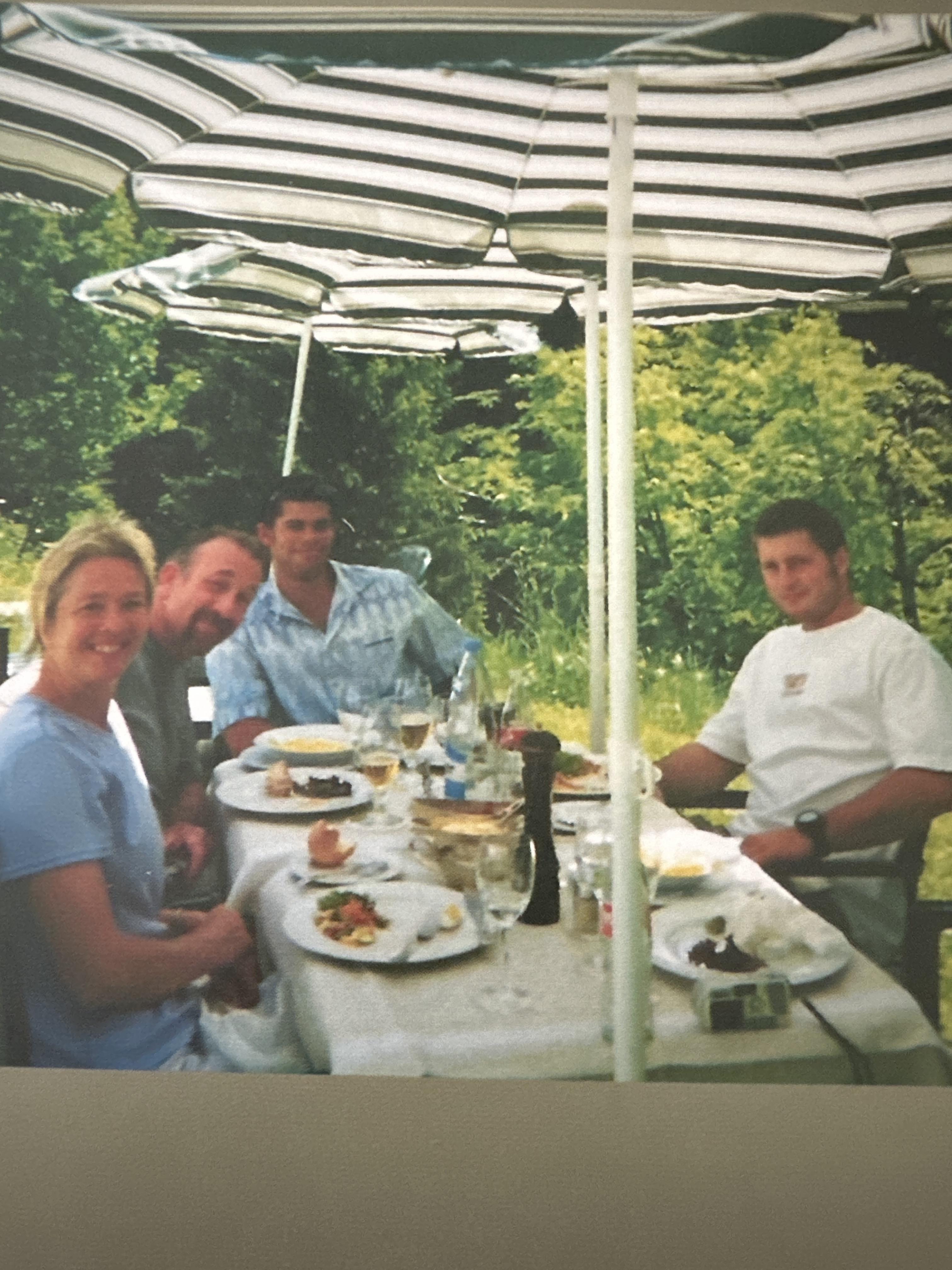 A group of four friends gather around a table covered in food, enjoying a sunny day together.