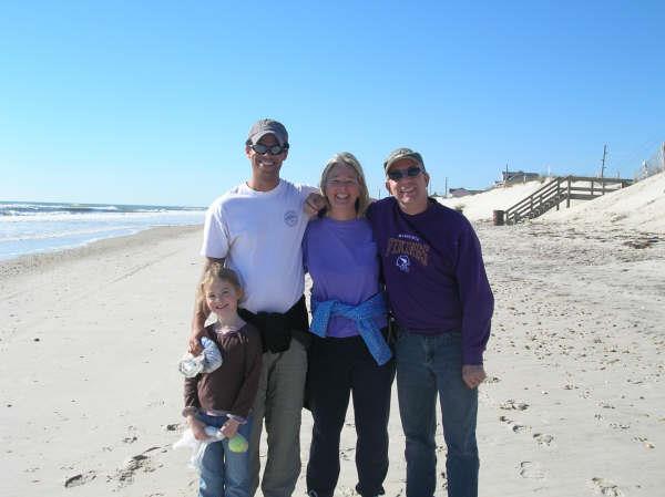 Four family members stand together on a sandy beach, enjoying the sunny weather and ocean view.