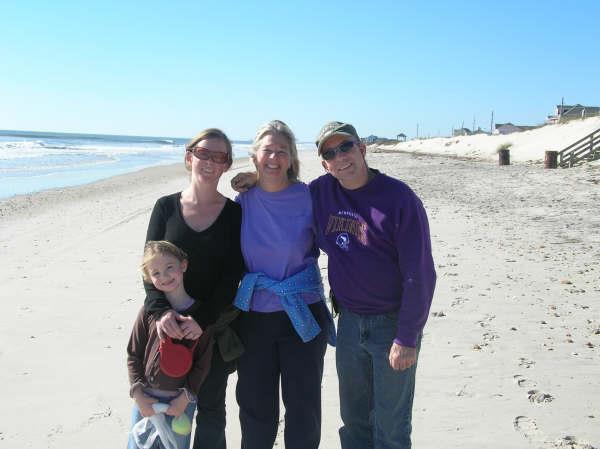 Family poses together on a beach with golden sand and a bright sunny sky overhead.