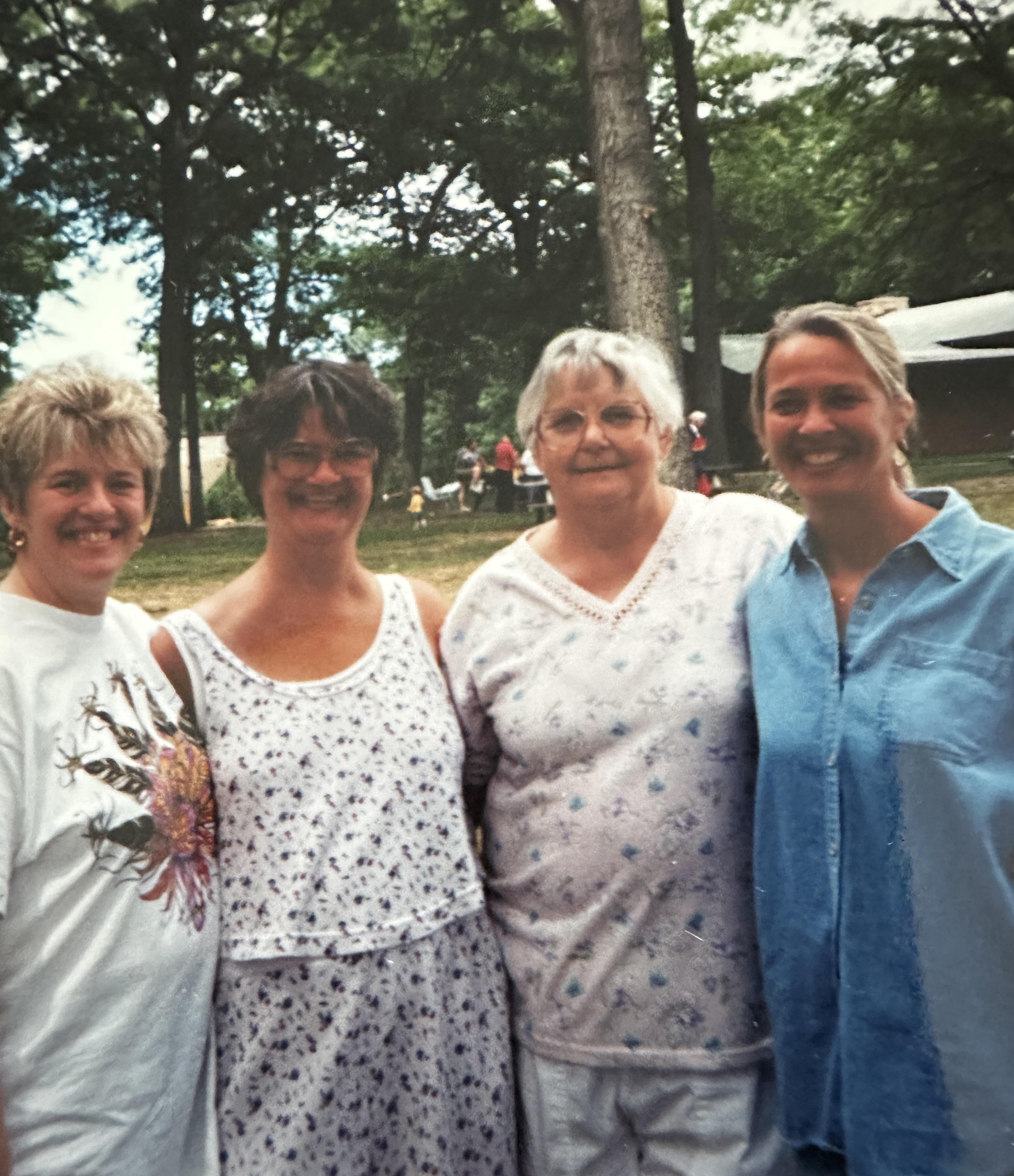 Four friends gather outdoors for a joyful picnic in a green park, sharing laughter in summer.