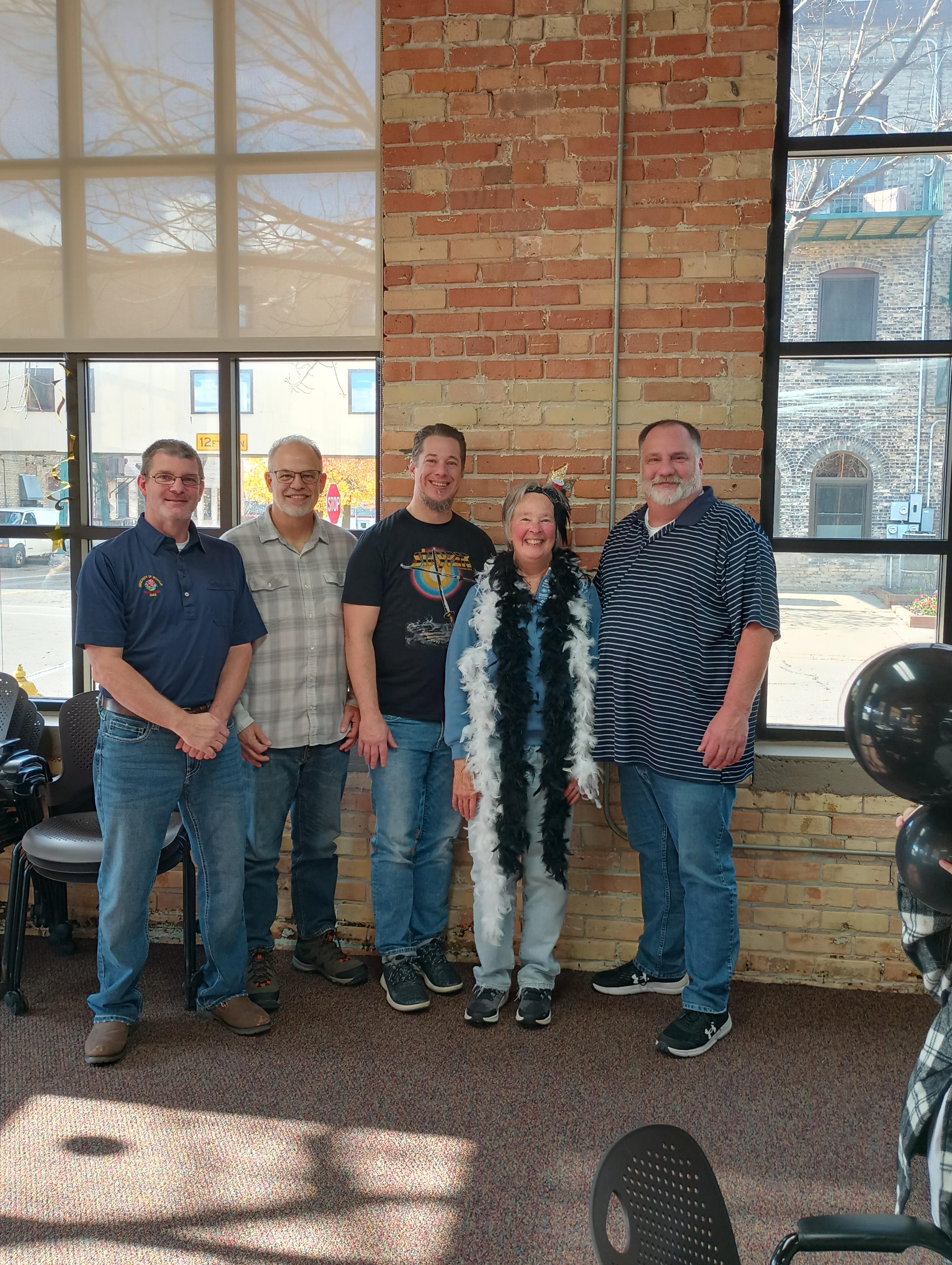 Friends gather and pose happily together in a cozy, well-lit space by large windows.