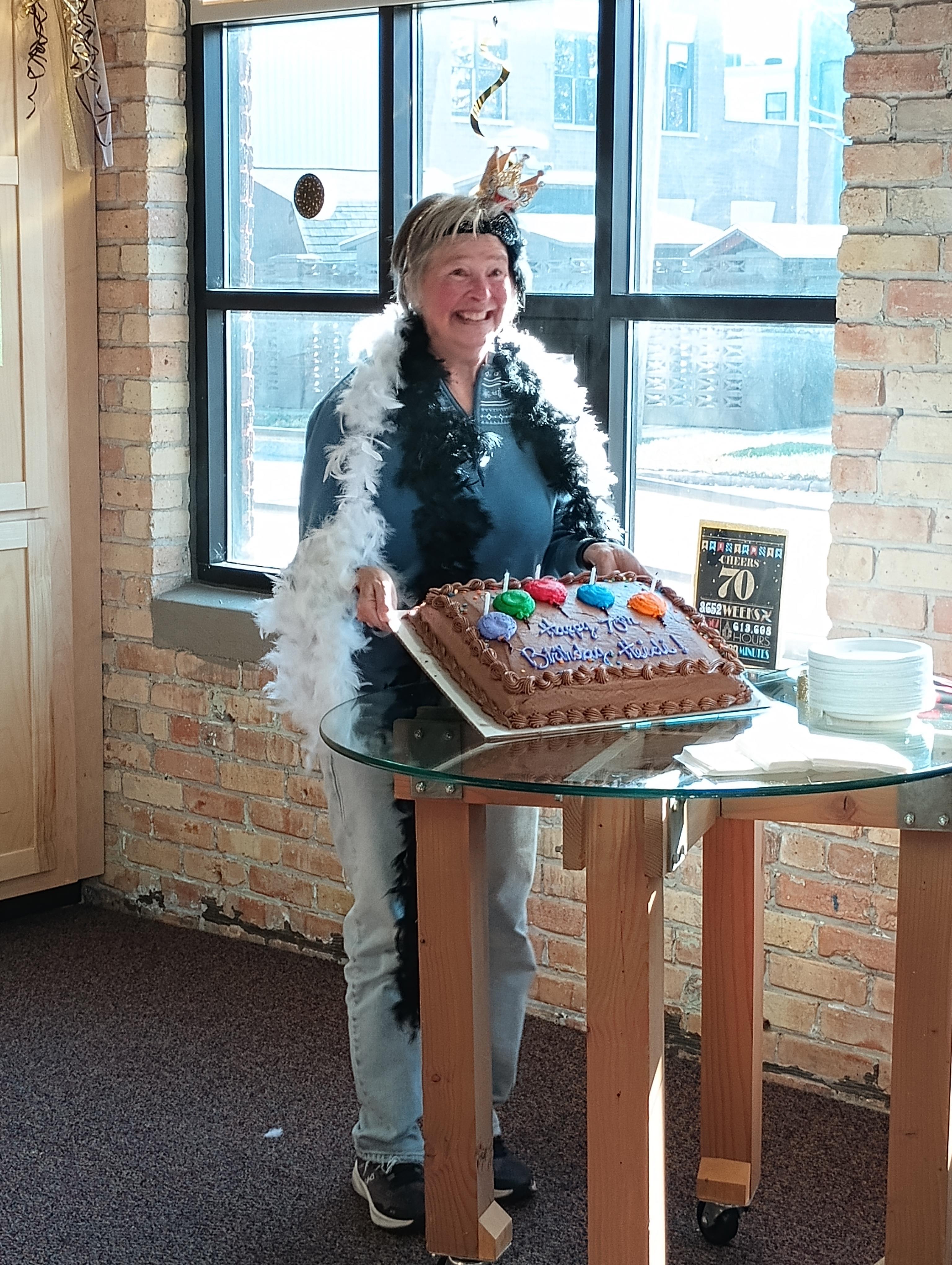 A woman stands proudly beside a beautifully decorated cake in a festive setting.