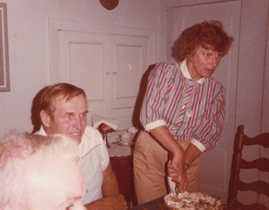 A warm family gathering features a woman serving food as a man smiles and enjoys the atmosphere.