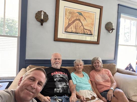 Four family members relax together on a couch, enjoying each other's company in a bright room.
