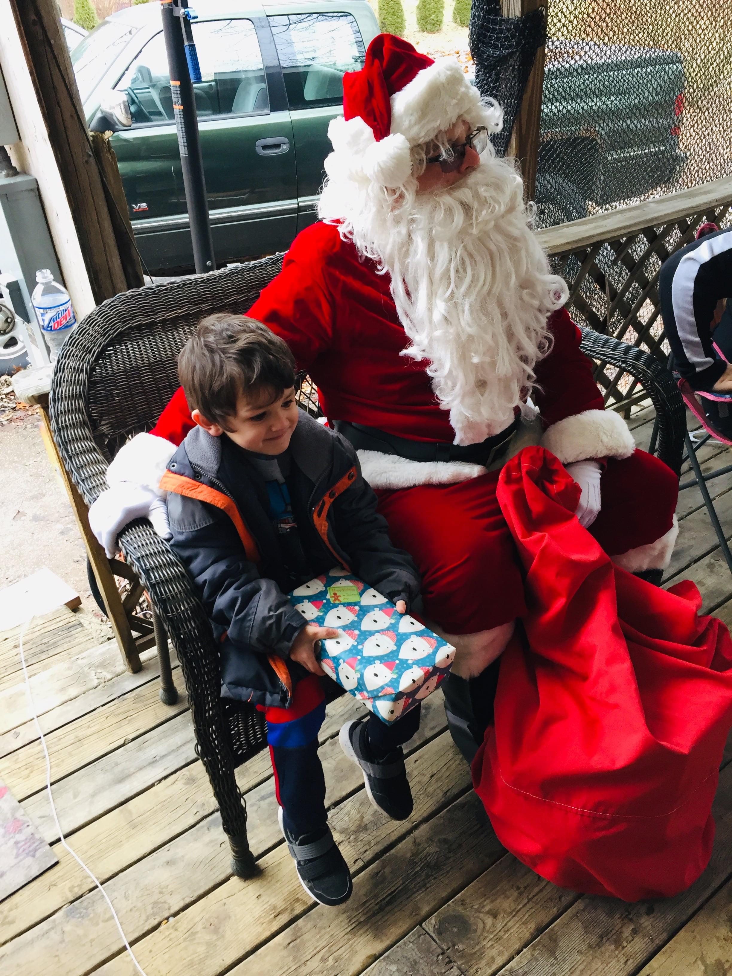 A cheerful young boy holds a gift while sitting next to Santa in a cozy setting.