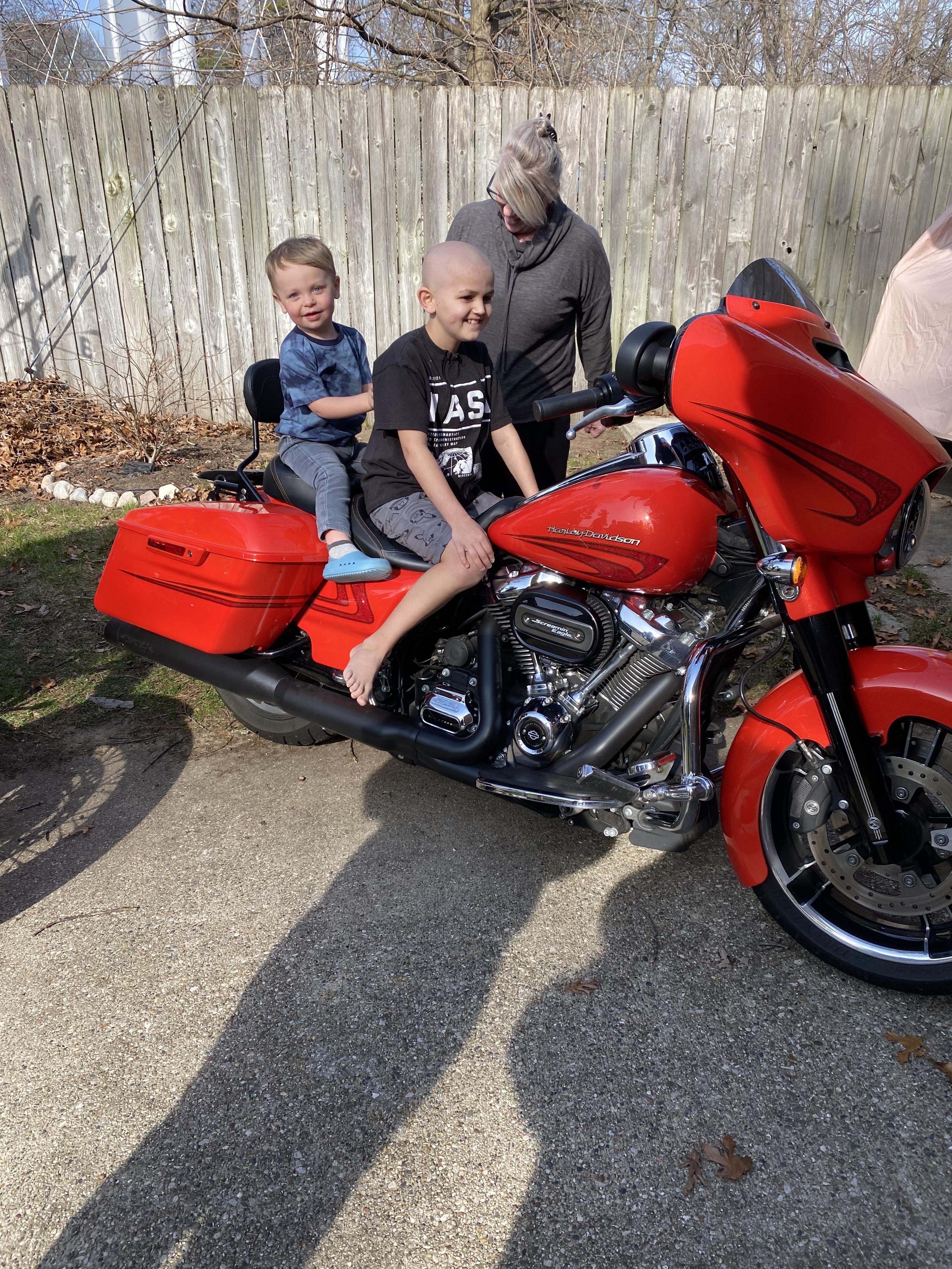 Two boys are sitting on a vibrant red motorcycle outside, smiling and enjoying the moment.