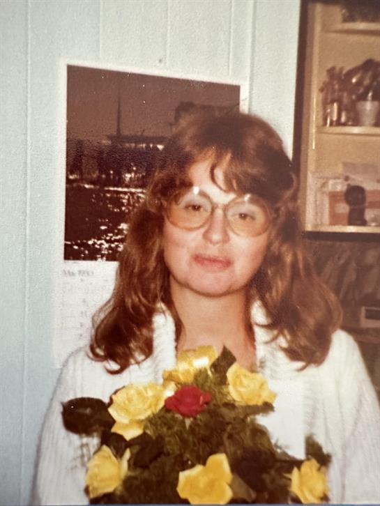 A woman smiles while holding a vibrant bouquet of yellow roses indoors, surrounded by warm decor.