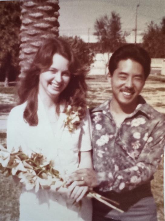 A joyful couple stands together, holding flowers in a park on a sunny day.