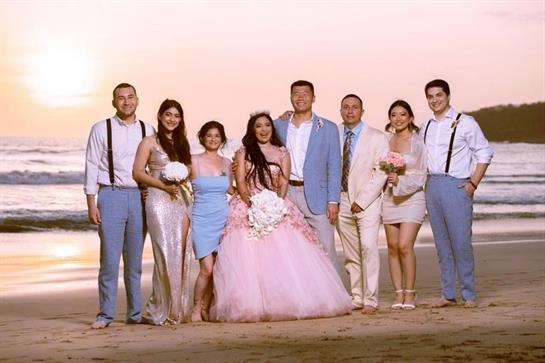 Family and friends gather on the beach at sunset to celebrate a wedding, surrounded by ocean waves.