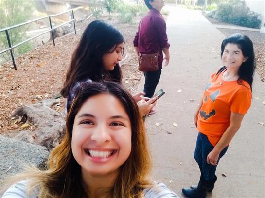 Group of friends laughing and chatting while taking a selfie in a park during a sunny day.