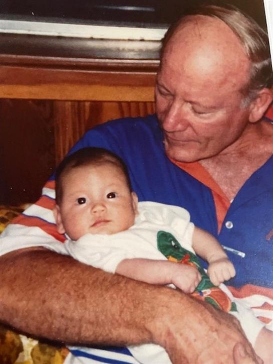 A grandfather lovingly gazes at his baby grandchild while holding them in a warm environment.