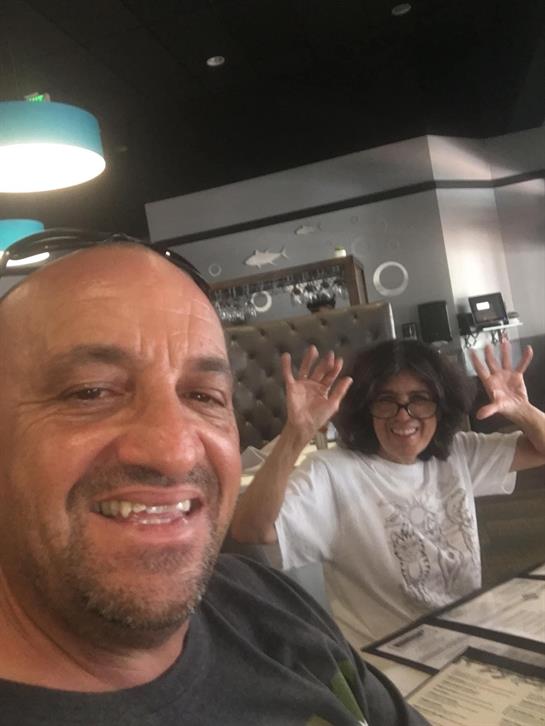 Two friends pose with big smiles at their table while enjoying lunch at a lively restaurant.