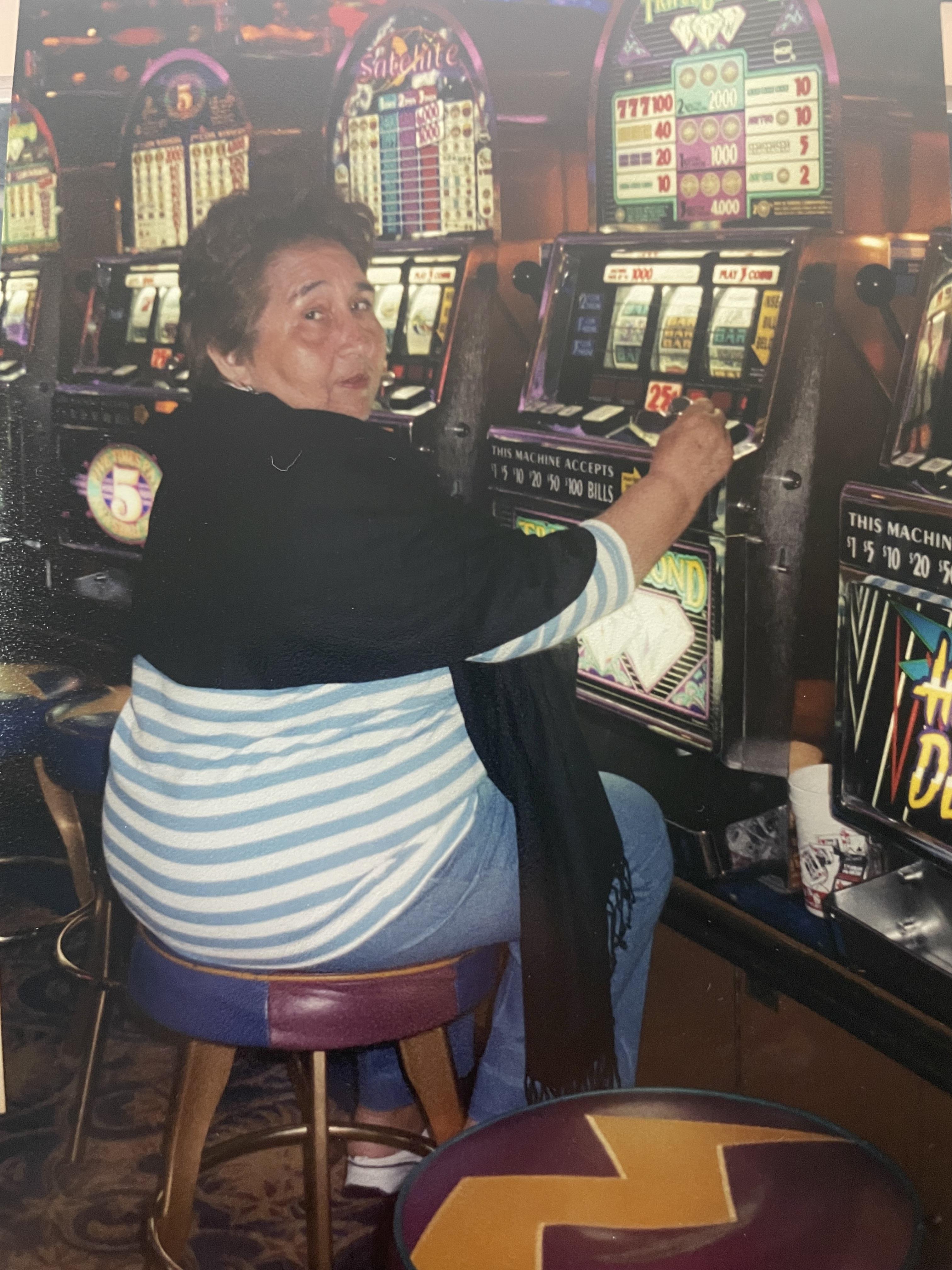 An elderly woman sits at a slot machine in a lively casino, pulling the lever with excitement.