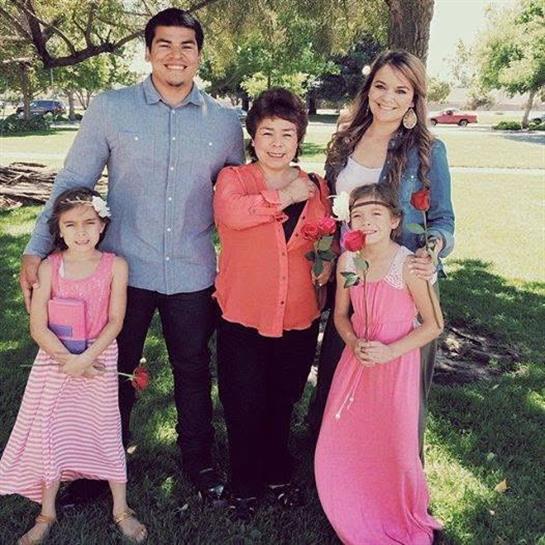 A family stands together in a park, celebrating with smiles and colorful clothing under a sunny sky.
