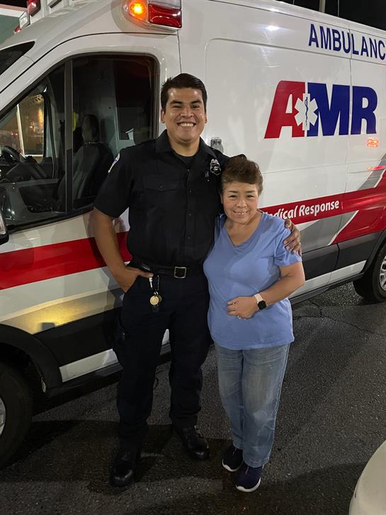 Two emergency responders smile together near an ambulance at night after assisting in a call.