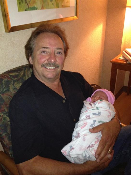 Smiling grandfather cuddles his newborn grandchild in a warm, inviting hospital room.