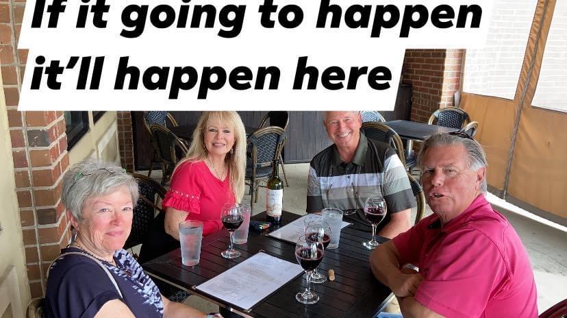 Friends gather around a table, enjoying wine and lively conversation in an outdoor setting.