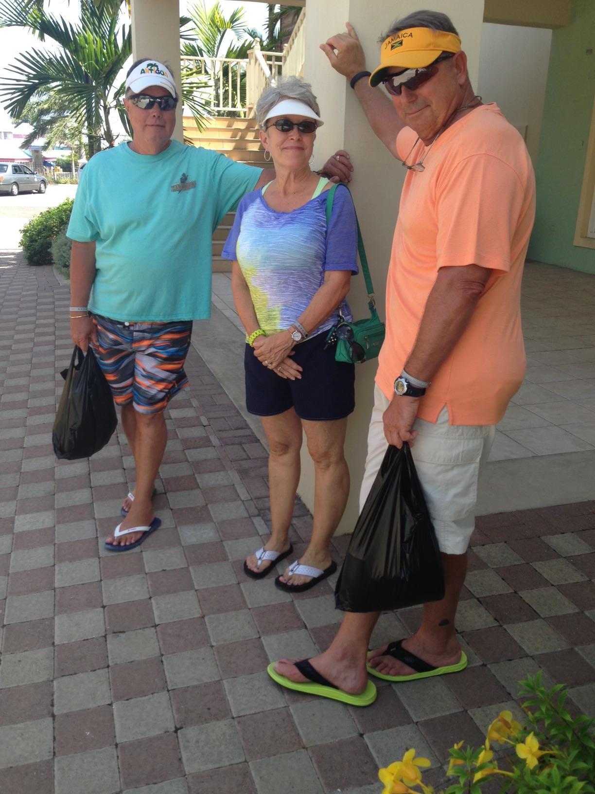 Three friends pose with bags outside a coastal building on a bright sunny day.