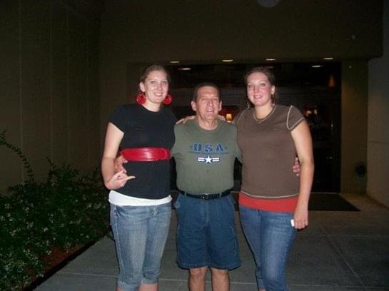 Three friends stand together outside a venue, smiling and enjoying each other's company at night.