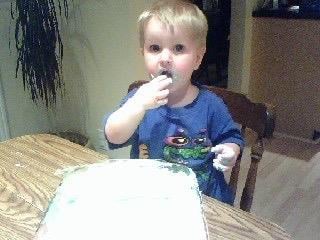 Bright-eyed toddler happily samples frosting from a birthday cake at home, spreading joy.