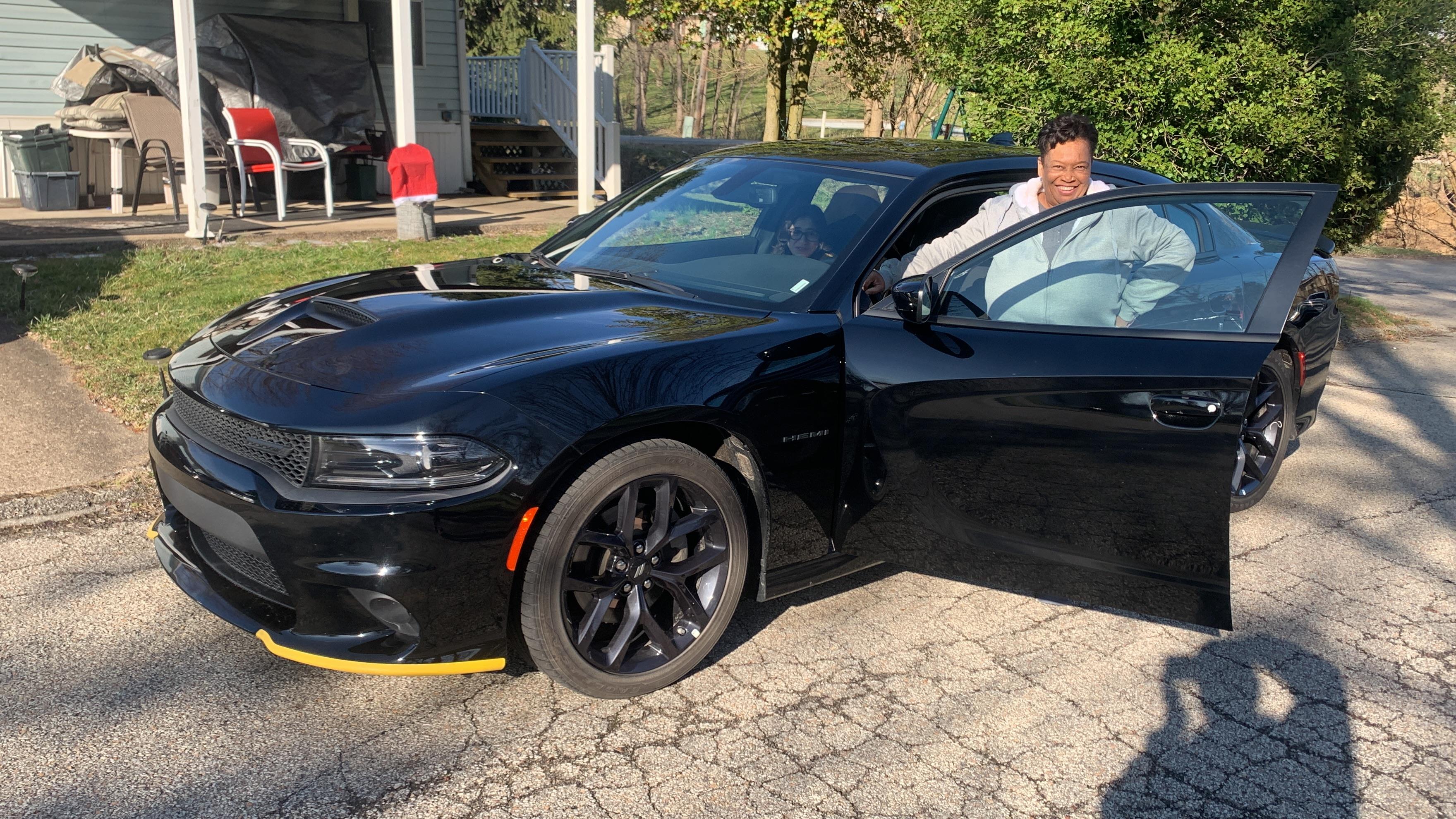 Man approaches a sleek black car parked near a house on a sunny day.