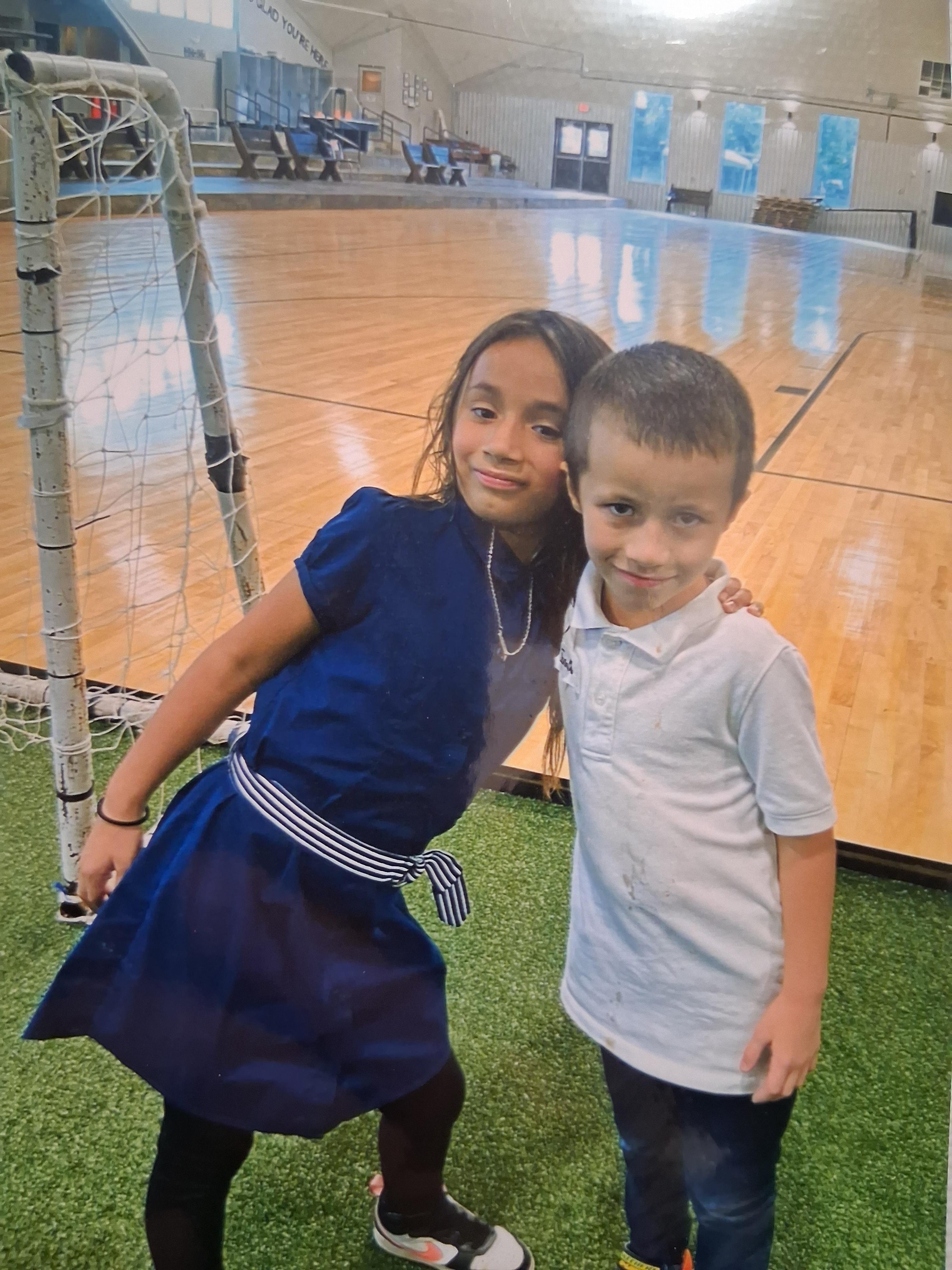 Two children pose happily for a photo in a vibrant indoor sports complex filled with energy.