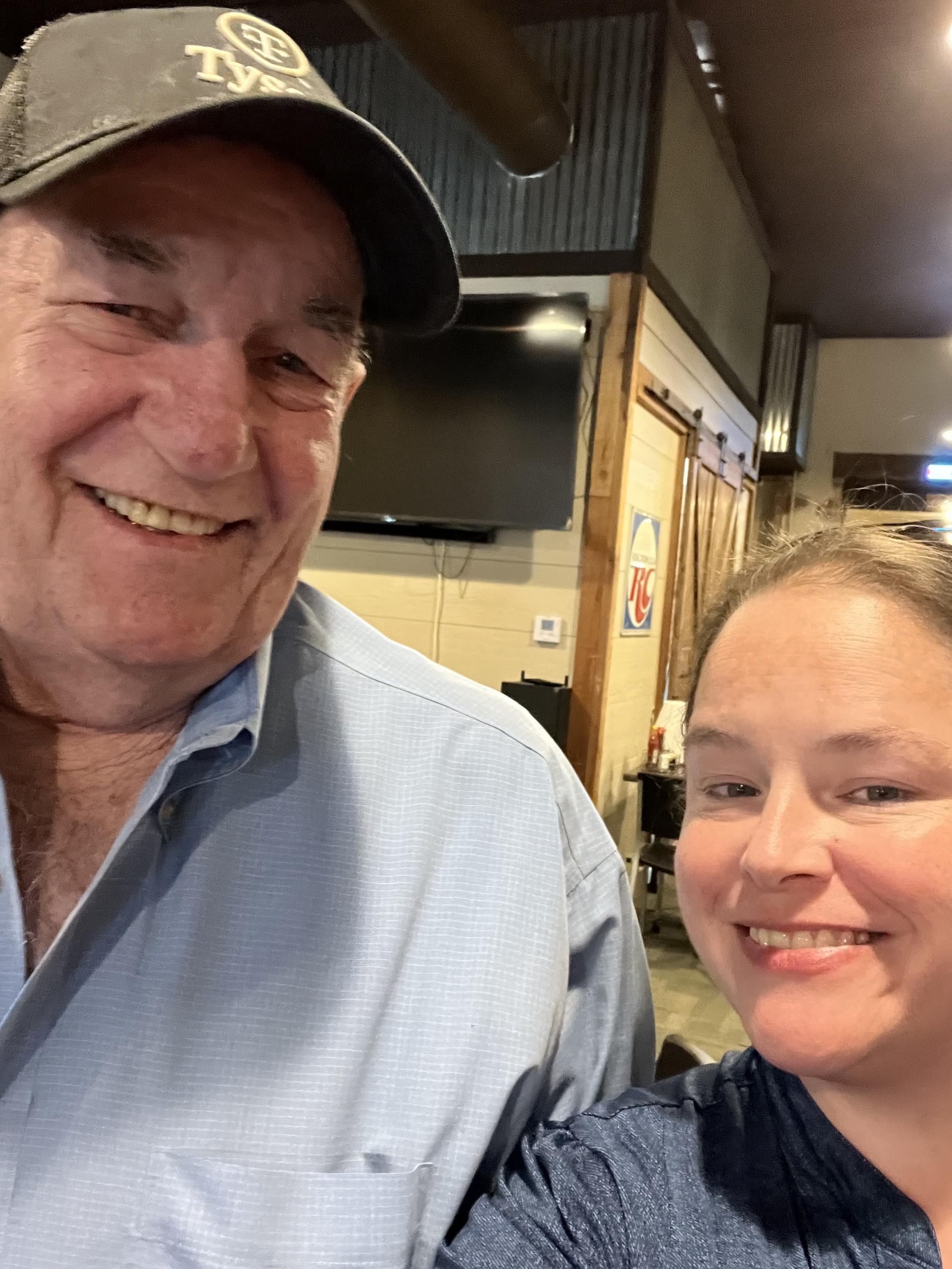 Two individuals smile joyfully while posing for a selfie in a casual dining location.