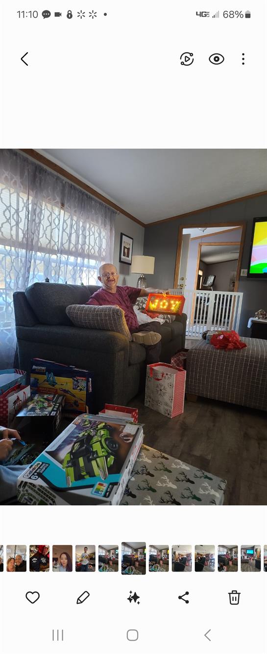 A man sits on a couch holding a bright sign showing the year while surrounded by gifts.