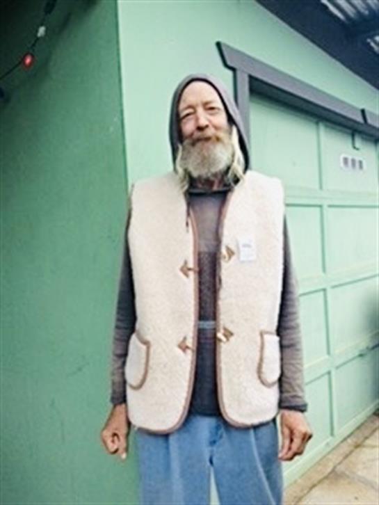 Older man with a beard smiles warmly while wearing a comfortable vest and casual clothes.