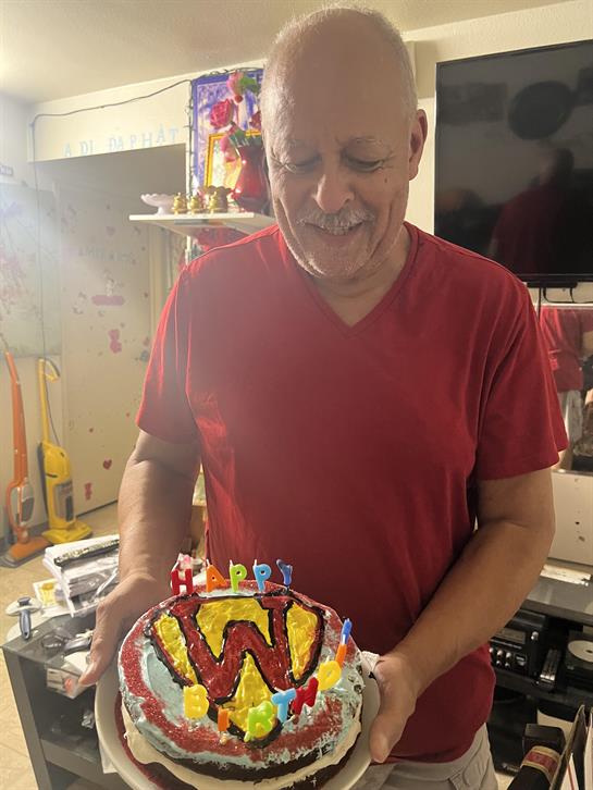 A man smiles while holding a festive cake adorned with candles, celebrating a birthday.
