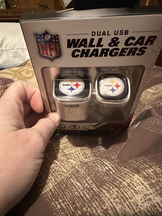 A hand displays NFL-themed chargers while resting on a patterned surface at home.