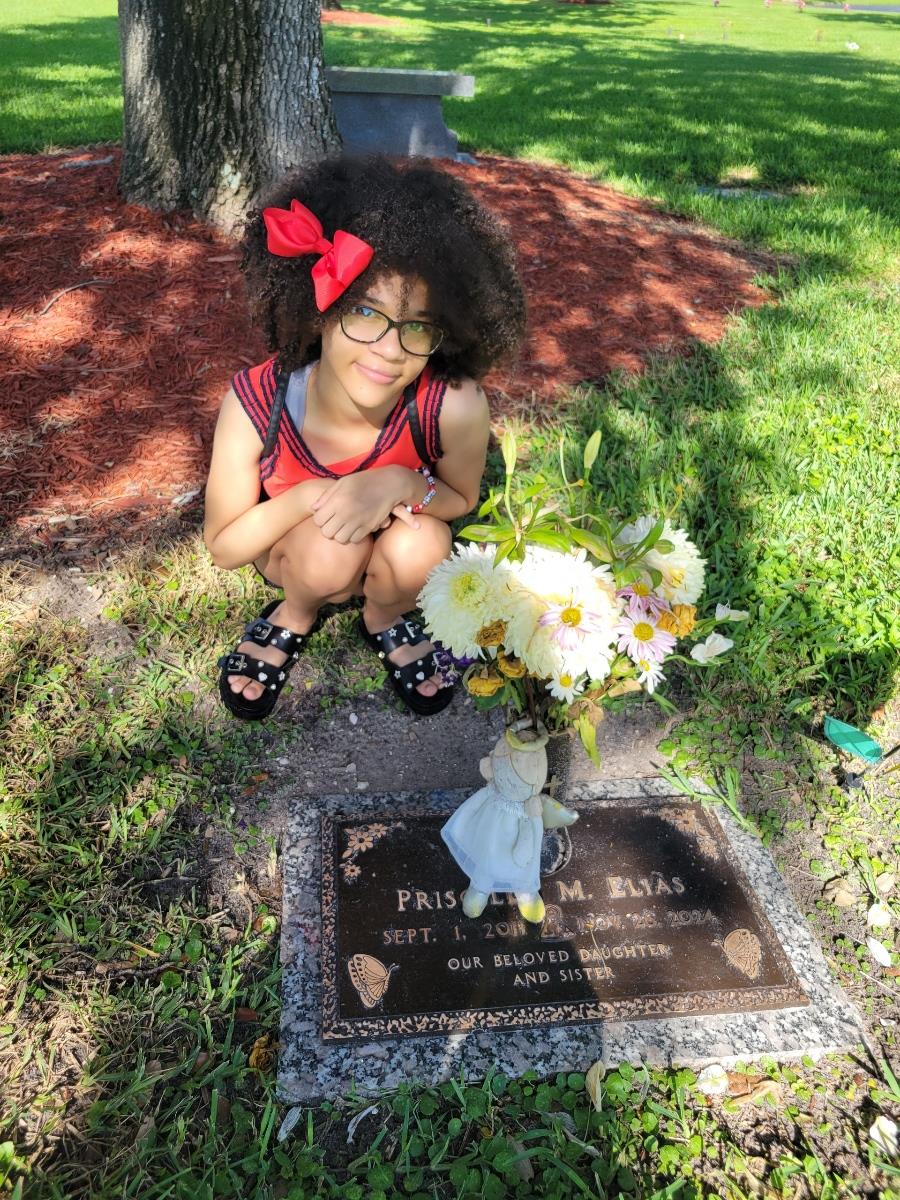 Girl kneels beside a grave marker, placing flowers with care in a peaceful outdoor space.