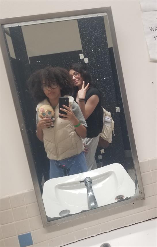 Friends pose for a fun selfie in a school restroom, showing smiles and camaraderie.