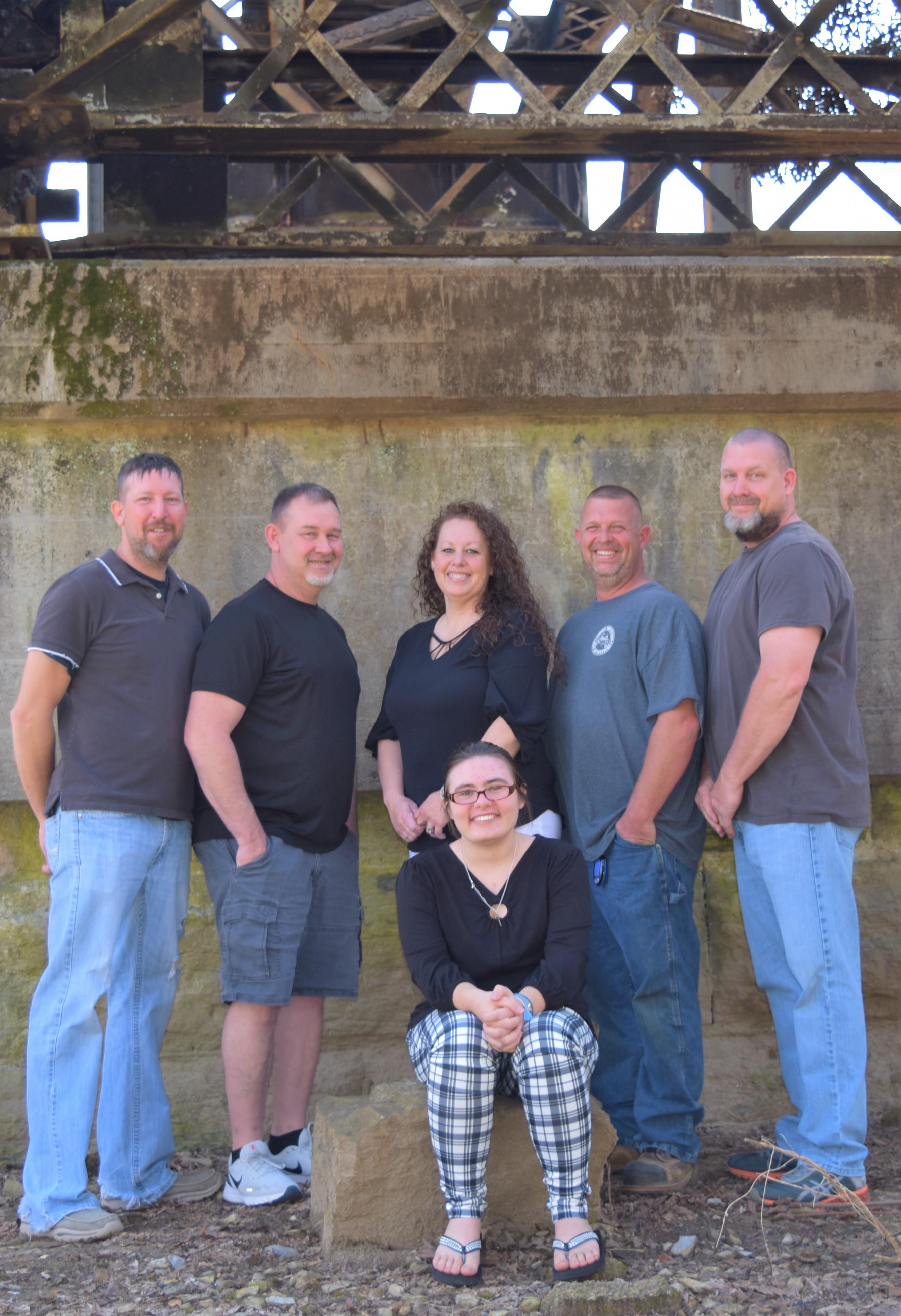 Group of six family members posing together in casual outfits beneath a concrete structure.