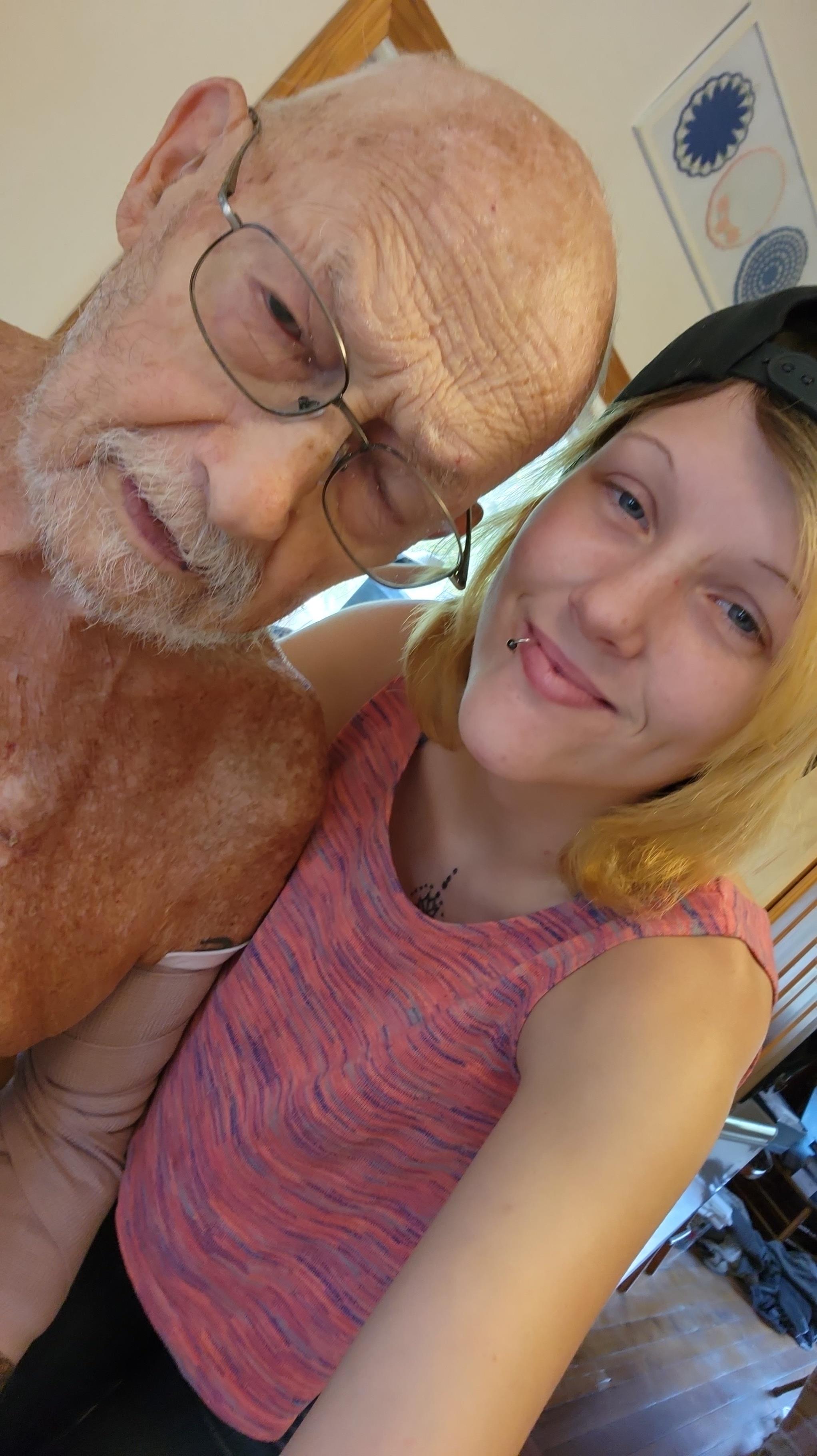 Elderly man poses affectionately with a young woman in a comfortable indoor space.