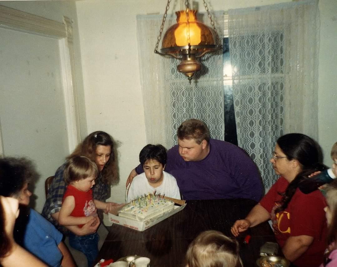 Children and adults joyfully gather around a birthday cake, excited for the celebration.