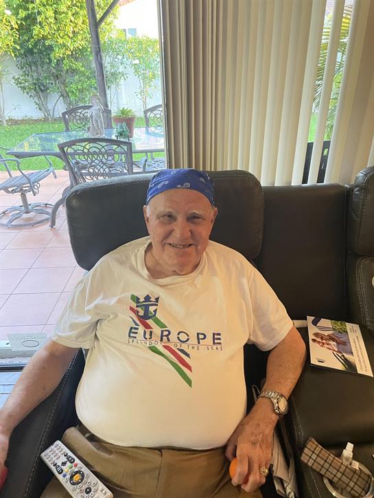 A cheerful elderly man relaxes in a cozy living room wearing a blue bandana and casual attire.