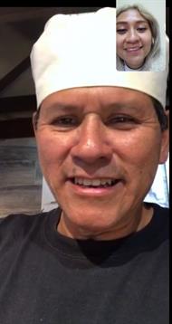 Chef wearing a white hat happily connects with a friend via video call showing a cozy atmosphere.