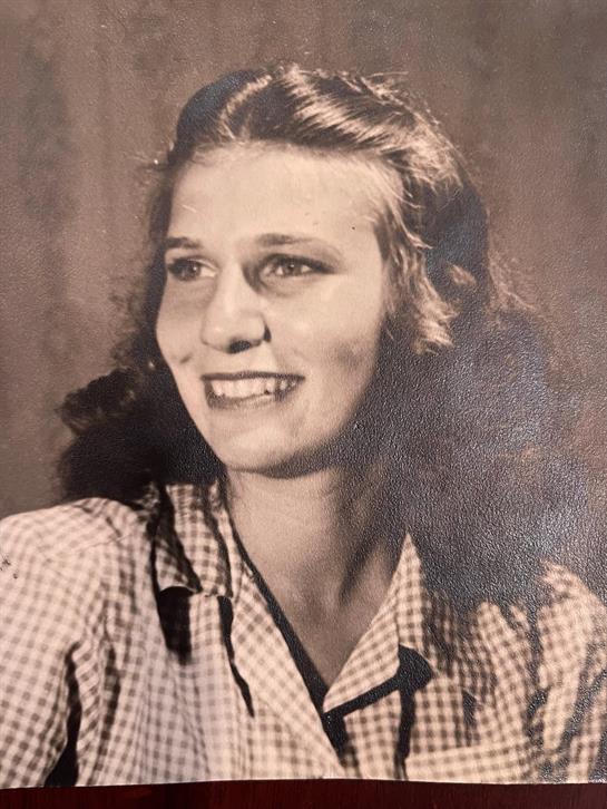 A cheerful young woman poses with a bright smile, showcasing her curly hair and checkered shirt.