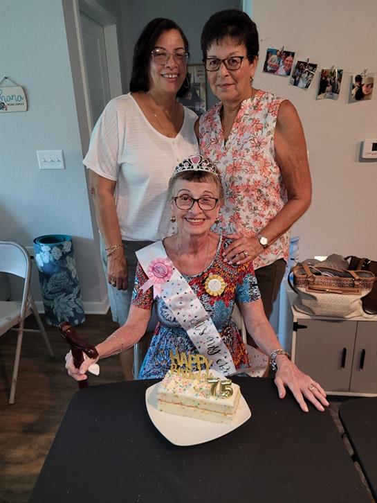 Family members commemorate a 75th birthday with cake and smiles in a warm interior.