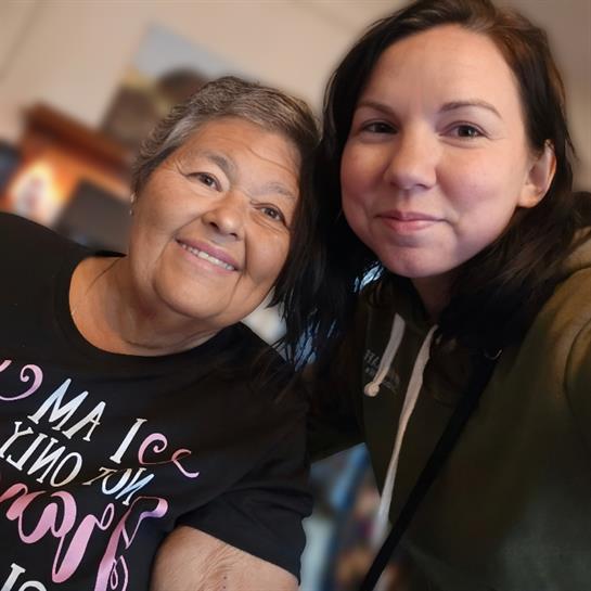 A granddaughter and her grandmother share a warm smile while posing for a selfie indoors.