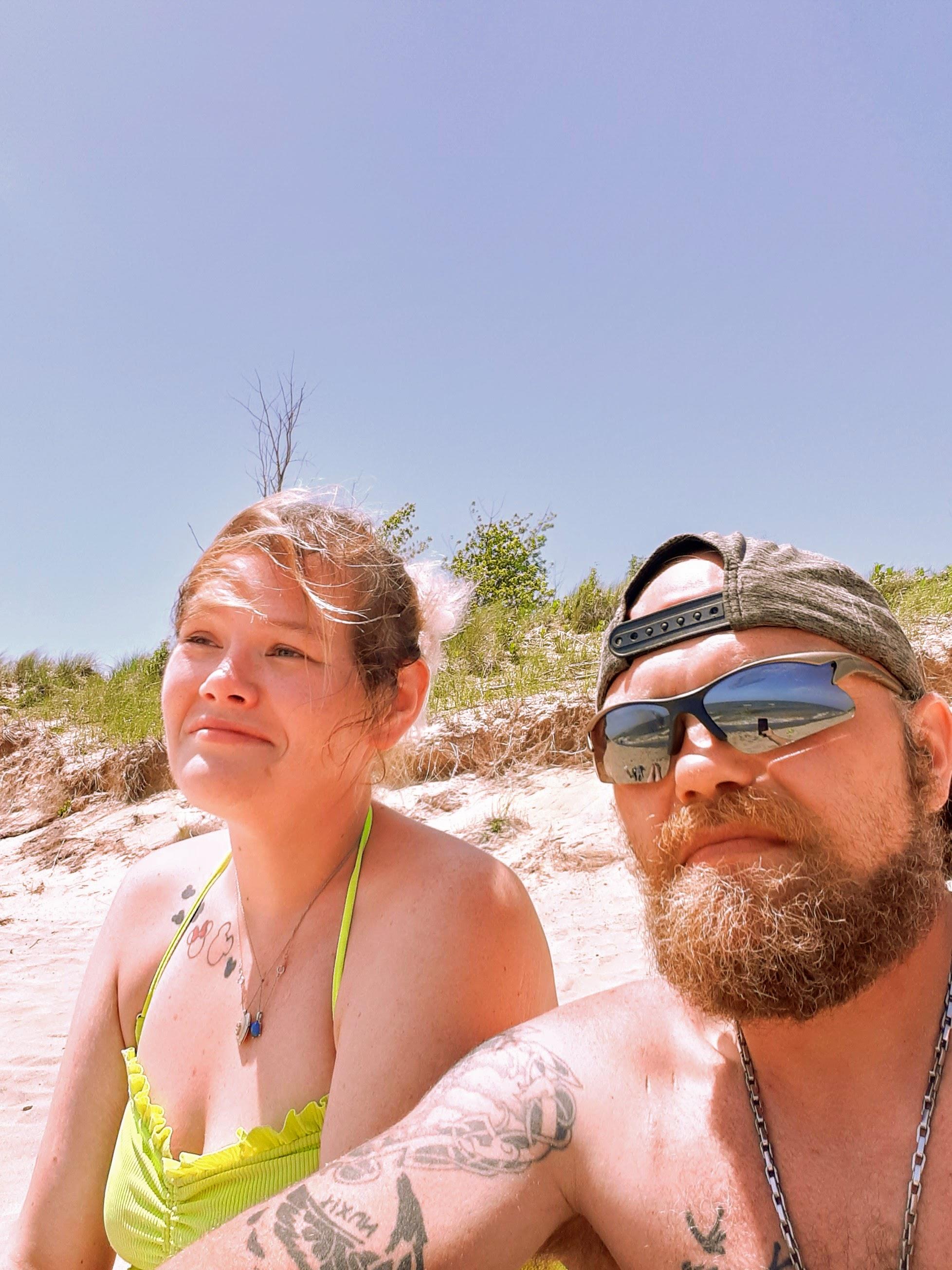 Two people relax on the beach, basking in the sun with clear blue skies overhead.